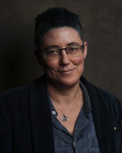 Headshot of Juliet, who is wearing glasses and a jacket over a shirt, and smiling slightly